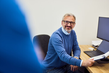 Professional Man Sitting at Desk Holding Document in Modern Office Setting