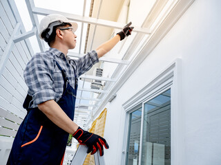 Asian male foreman or construction worker climbing up on an aluminium ladder pointing at the roof...