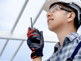 Confident Asian man engineer talking on walkie talkie while looking at roof structure. Smart...