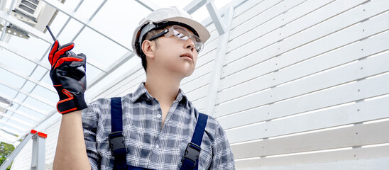 Asian man engineer holding walkie talkie using for cooperate with worker team while looking at...
