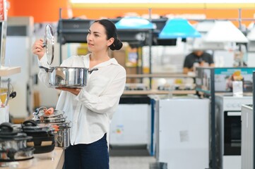 Pretty, young woman choosing a the right pot for her cooking in a modern home furnishings store