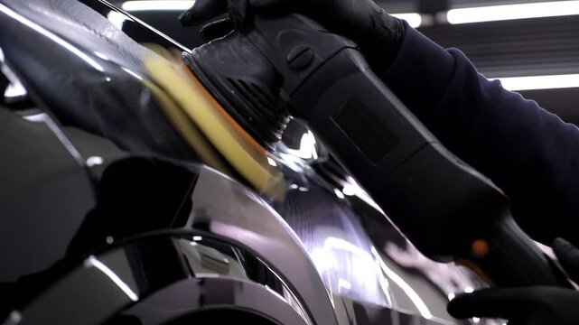 A man polishes a black car with a polishing machine in a car dealership. Car care in an auto repair shop.