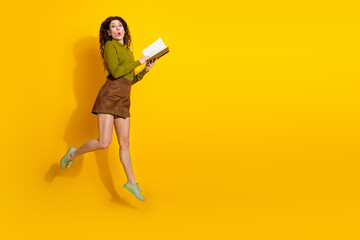 Joyful young woman jumping with a book against a vibrant yellow background, showcasing a cheerful...