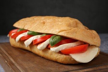 Tasty sandwich with mozzarella cheese, tomatoes and basil on grey table against black background,...