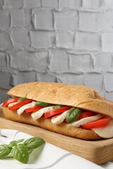 Tasty sandwich with mozzarella cheese, tomatoes and basil on table against grey textured wall,...