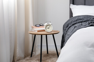 Bedside table with alarm clock, books and glasses near bed indoors