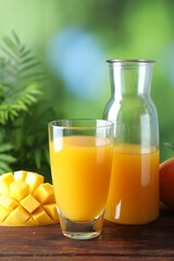 Tasty mango juice in glass, carafe and fresh fruit on wooden table against blurred background