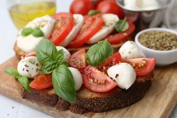 Tasty sandwiches with mozzarella cheese, tomatoes, basil and spices on light table, closeup
