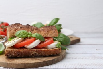 Tasty sandwich with mozzarella cheese, tomatoes and basil on white wooden table, closeup. Space for text