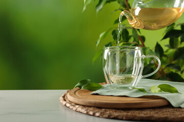 Pouring tasty green tea into cup at white marble table outdoors, closeup. Space for text