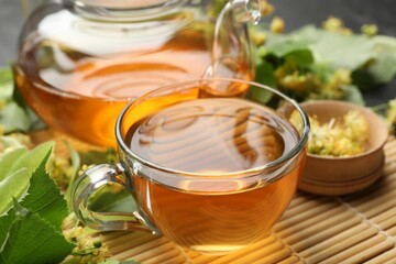 Tasty linden tea in cup, teapot, leaves and flowers on table, closeup
