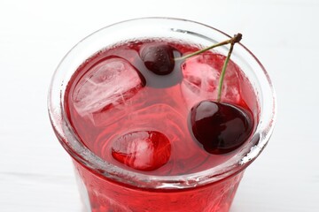 Tasty cherry soda with ice cubes and berries on white wooden table, closeup
