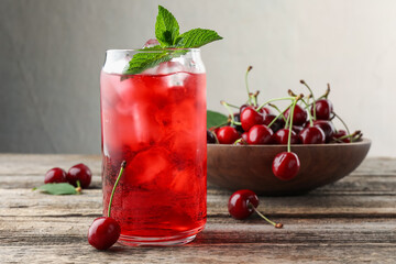 Tasty cherry soda with ice cubes, berries and mint on wooden table, closeup
