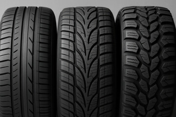 Set of three new car tires standing on grey background showing different treads