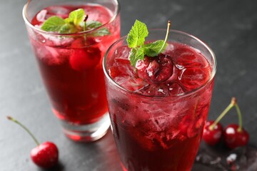 Tasty cherry soda with ice cubes, berries and mint in glasses on grey table, closeup