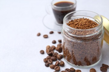 Instant coffee in glass jar, beans and hot drink on light grey table, closeup. Space for text