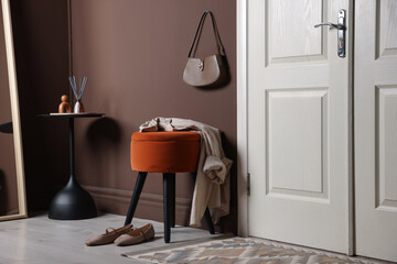 Stylish pouf with shirt and shoes near door at home