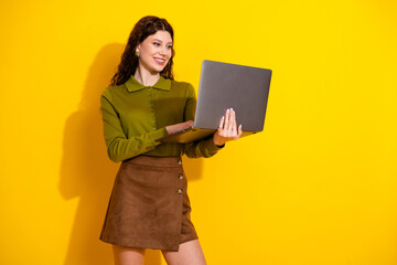 Charming woman in casual outfit holding a laptop with a yellow background demonstrating style,...