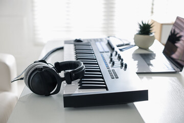 MIDI keyboard, headphones and laptop on white wooden table indoors, closeup