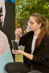 Young adult female with brown hair deeply focused on outdoor painting. Casual attire, serene...