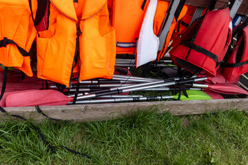 Close-up of colorful paddles and life jackets stored together on a wooden rack