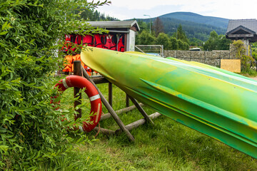 Stacked green kayaks near a red lifebuoy on a stand