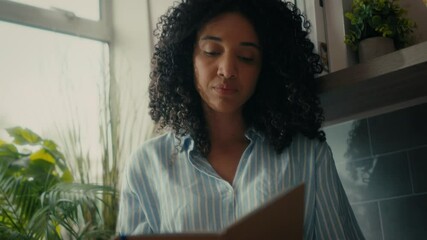 A woman with curly hair in a cosy kitchen, writing in her notepad. - Powered by Adobe
