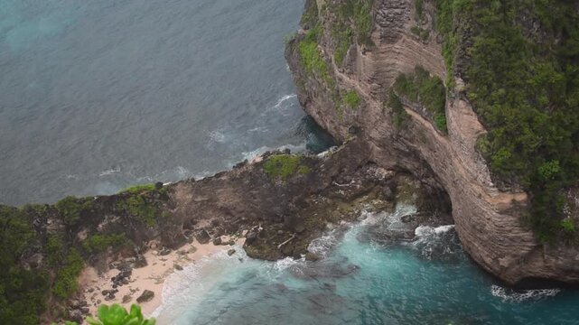 Dramatic cliffside view of Kelingking Beach in Nusa Penida, Bali &ndash; showcasing the raw beauty of turquoise waves crashing against the rugged shoreline.