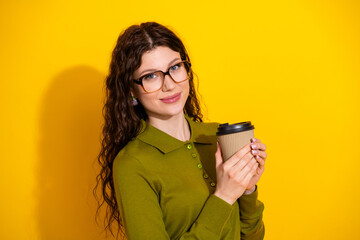 Trendy young woman with glasses holding a coffee cup against a vibrant yellow background showcasing...