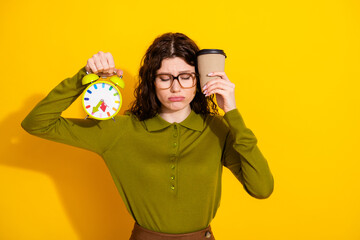 Young female holding a colorful clock and coffee cup against a vibrant yellow background,...