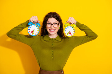 Young woman holding colorful retro alarm clocks on a yellow background, expressing modern fashion...