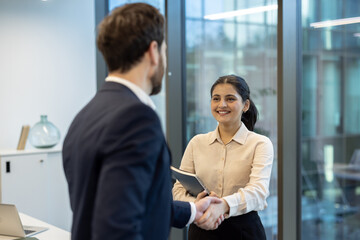 In an office setting, a man and woman shake hands, likely after a successful meeting or agreement.