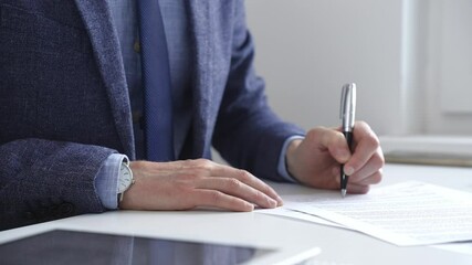 Professional businessman signing contract with silver pen, wearing tailored suit, business documents and digital tablet nearby. Business people concept - Powered by Adobe