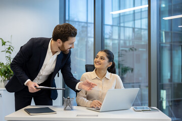 A businessman guides and advises a businesswoman while working on a laptop in a modern office...