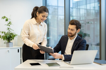 A woman presents a document to a man, both smiling in a modern office setting.