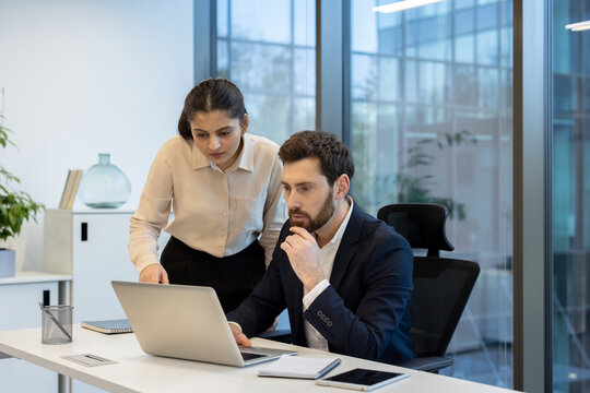 A diverse business team collaborates over a laptop in a modern office setting, discussing data and strategy.