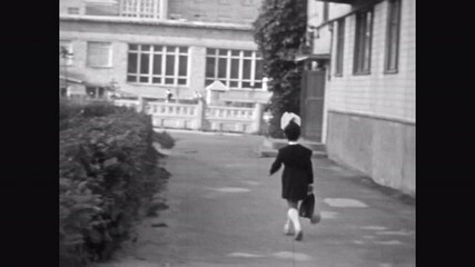Little schoolgirl girl walking to primary school. Child pupil with bow wearing Soviet school uniform carrying school bag in street. Archival retro film. Back to school. Vintage 1960s archive education