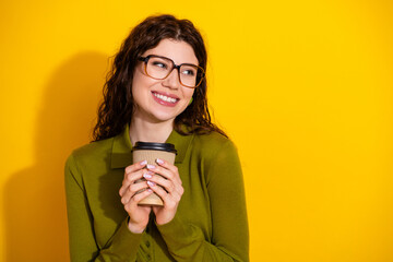 Young cheerful woman wearing glasses holding a coffee cup on a stylish yellow background, radiating vibrant positivity