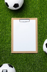 A soccer balls and clipboard with white paper sheet on a green field. Top view, flat lay.