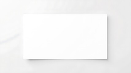 A blank white rectangular canvas or paper rests on a subtly textured light gray surface with soft shadows