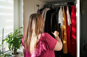 Woman is looking through her closet, which is full of clothes