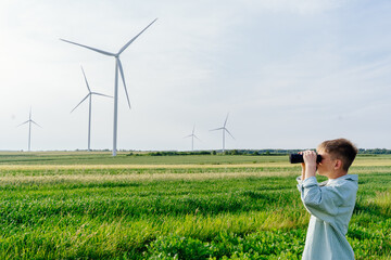 Teen boy in striped shirt and red shorts standing in green field with binoculars, looking at wind...