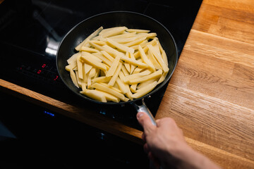 First-person view: man holding handle of pan filled with raw French fries on sleek black...