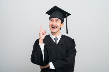 A young man in a graduation gown and cap smiles at the camera, striking a confident pose to...