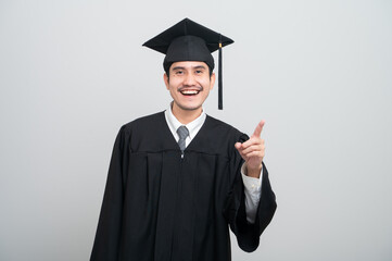 A young man in a graduation gown and cap smiles at the camera, striking a confident pose to...