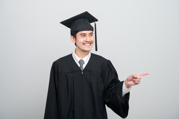A young man in a graduation gown and cap smiles at the camera, striking a confident pose to...