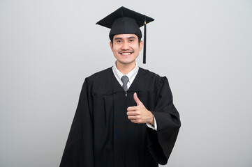A young man in a graduation gown and cap smiles at the camera, striking a confident pose to...