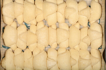 A close-up overhead shot shows rows of raw, pale yellow mini croissants sprinkled with sesame seeds on a grid surface