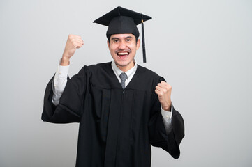 A young man in a graduation gown and cap smiles at the camera, striking a confident pose to...