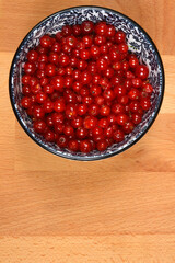 A top-down shot of a decorative blue and white bowl filled with vibrant red currants, placed on a light wooden surface with ample copy space below
